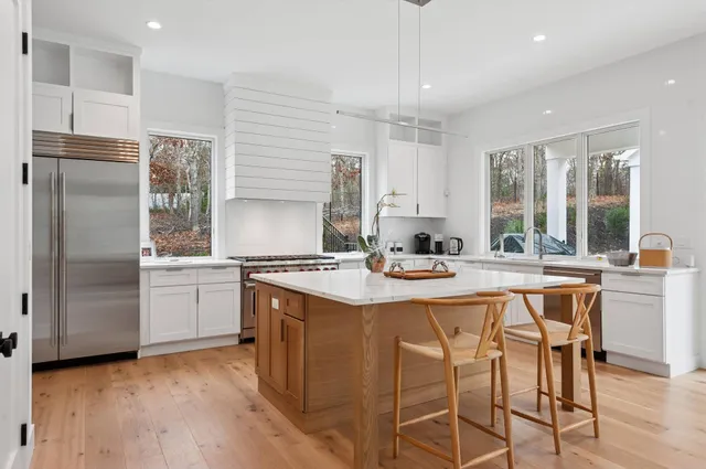 a kitchen with stainless steel appliances granite countertop a stove a sink a refrigerator and white cabinets with wooden floor