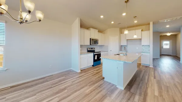 a view of an empty room and kitchen with wooden floor
