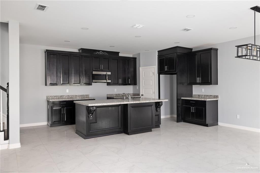 5307 North Crown Point Pharr, TX 78577 - Photo 3 of 11 Kitchen with dark cabinets, stainless steel microwave, an island with sink, and light marble finish floors
