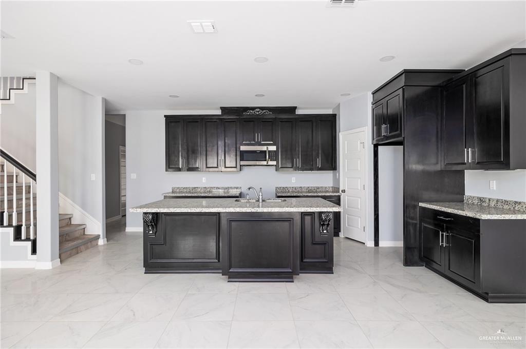 5307 North Crown Point Pharr, TX 78577 - Photo 4 of 11 Kitchen featuring dark cabinetry, light marble finish flooring, stainless steel microwave, and a center island with sink