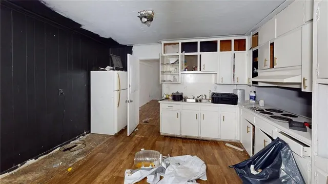 a kitchen with stainless steel appliances a white refrigerator a stove a sink and white cabinets with wooden floor