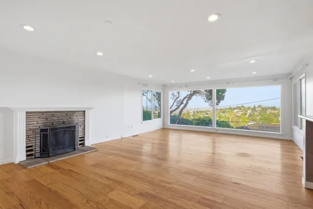 an empty room with wooden floor fireplace and windows