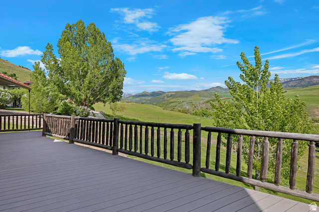 306 Spring Road Preston, ID 83263 - Photo 40 of 55 Expansive outdoor deck with gray composite decking and rustic wood railing, bordered by mature trees and verdant hills