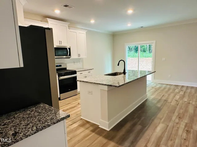 a kitchen with stainless steel appliances granite countertop a sink a stove a refrigerator a washer dryer and white cabinets