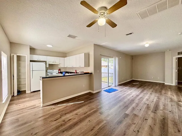 a view of an empty room and kitchen with wooden floor and a ceiling fan