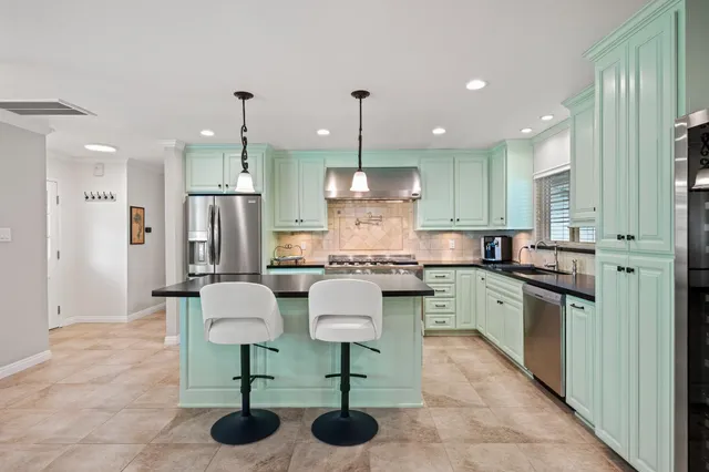 a kitchen with stainless steel appliances granite countertop a sink a stove a refrigerator cabinets and chairs