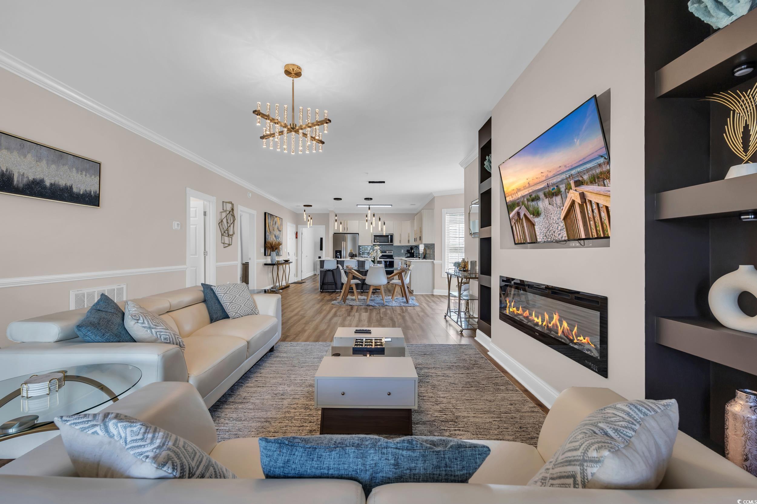 4821 Luster Leaf Circle, Unit 101 Myrtle Beach, SC 29577 - Photo 25 of 30 Living room with wood finished floors, a glass covered fireplace, a chandelier, and ornamental molding
