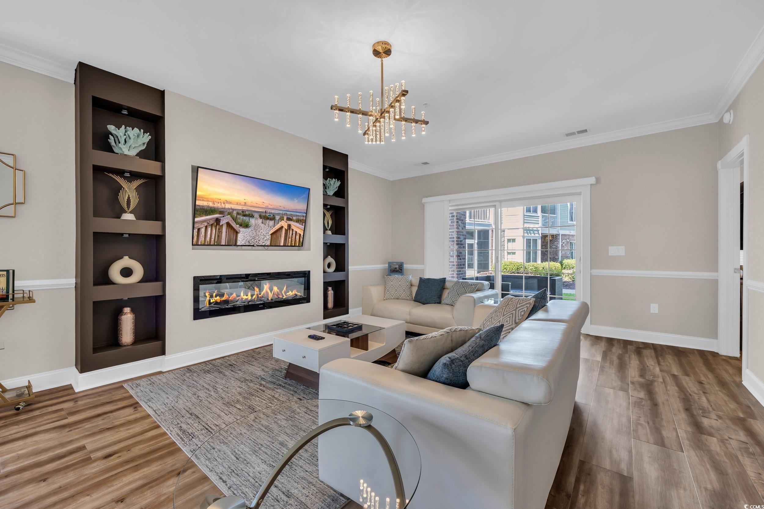 4821 Luster Leaf Circle, Unit 101 Myrtle Beach, SC 29577 - Photo 26 of 30 Living area featuring crown molding, built in features, a glass covered fireplace, wood finished floors, and a chandelier