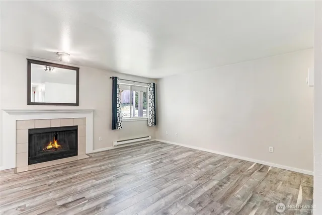 a view of an empty room with wooden floor fireplace and a window