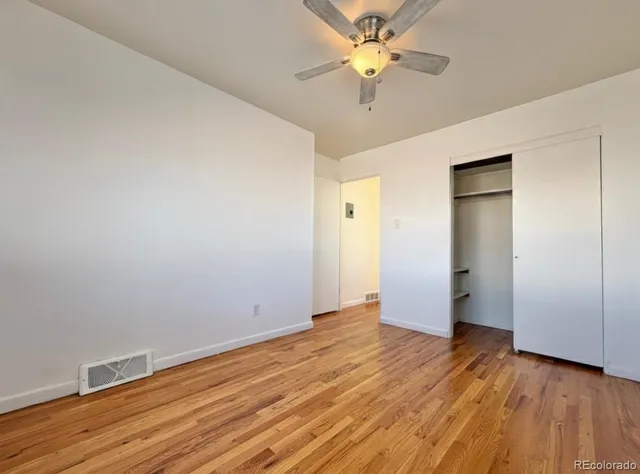 an empty room with wooden floor and a ceiling fan