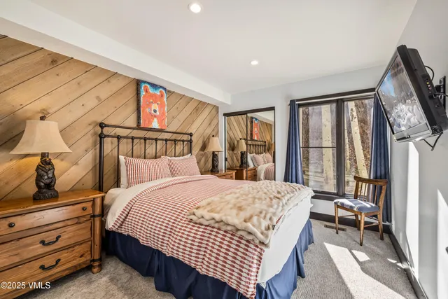 a bedroom with a bed a dresser and a large mirror next to a window