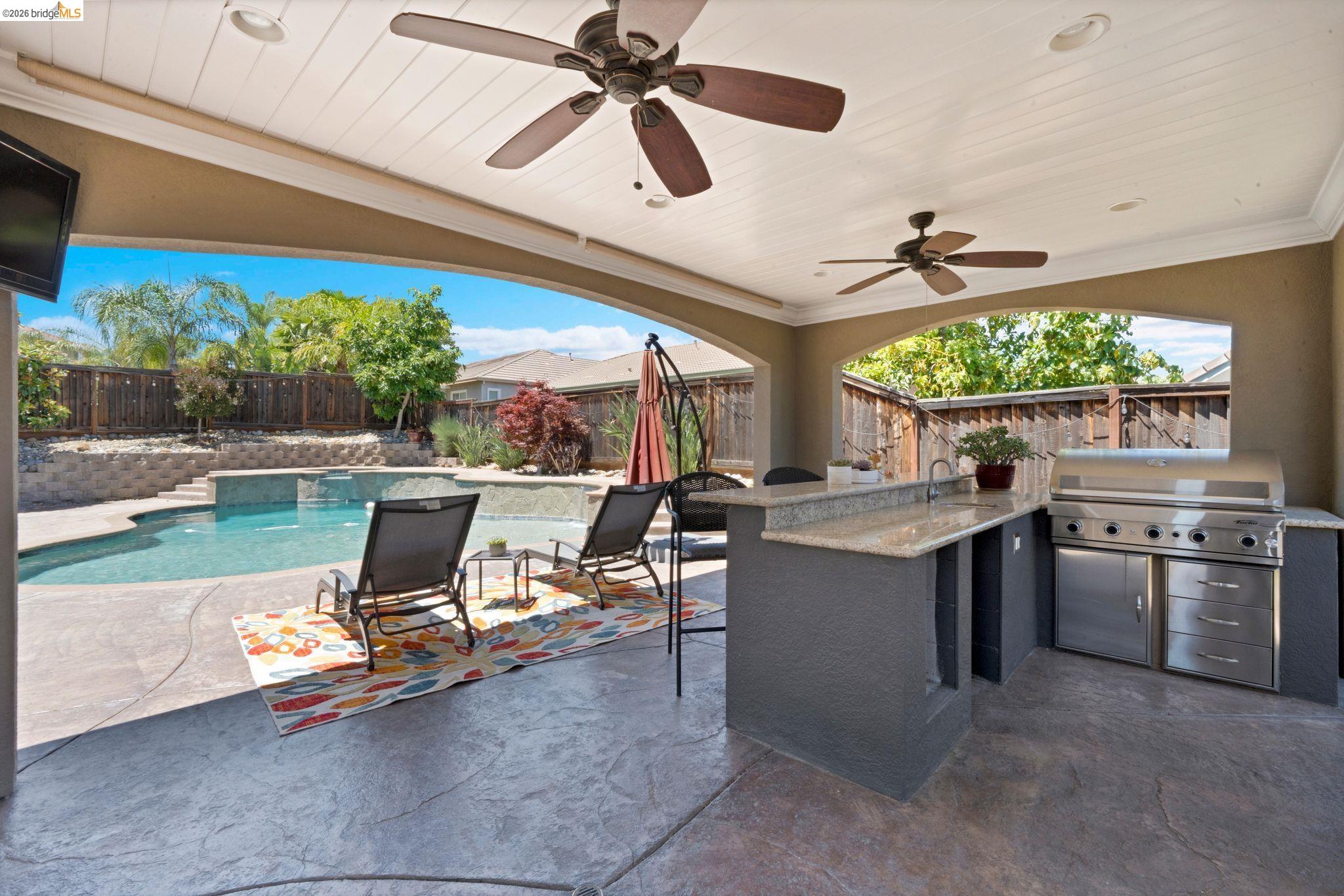 2513 Winged Foot Road Brentwood, CA 94513 - Photo 37 of 45 Covered patio featuring an outdoor kitchen with stainless steel appliances, a built-in swimming pool with an integrated spa, stamped concrete flooring, and a beadboard ceiling with ceiling fans