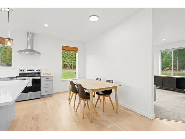 a kitchen with stainless steel appliances granite countertop a stove a refrigerator a sink a dining table and chairs with wooden floor