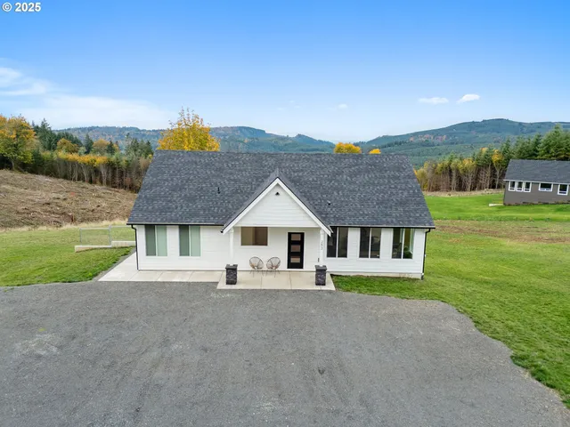 a house that is sitting in the grass with large trees and plants