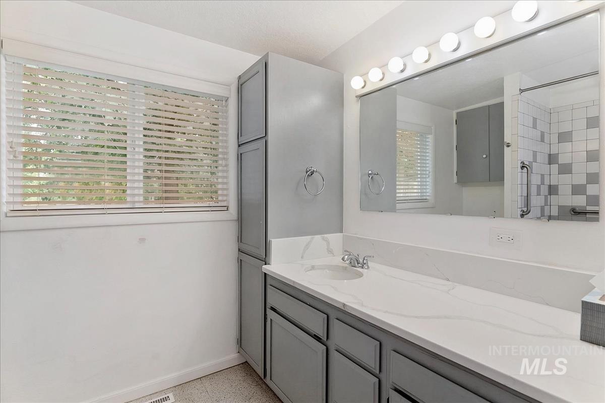 7141 West Hill Road Boise, ID 83714 - Photo 20 of 28 Bathroom featuring a built-in tub with shower, checkerboard wall tiling, and a vanity with a white countertop