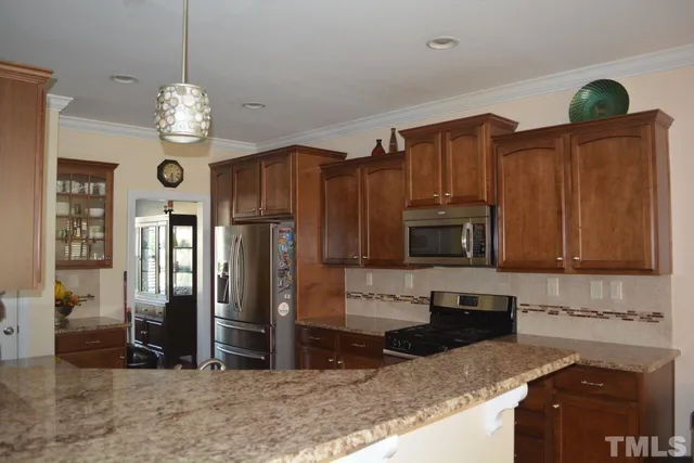 a kitchen with stainless steel appliances granite countertop a refrigerator a stove and a sink with wooden cabinets