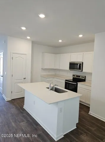 a kitchen with stainless steel appliances a sink a stove a microwave a refrigerator a white cabinets and wooden floor