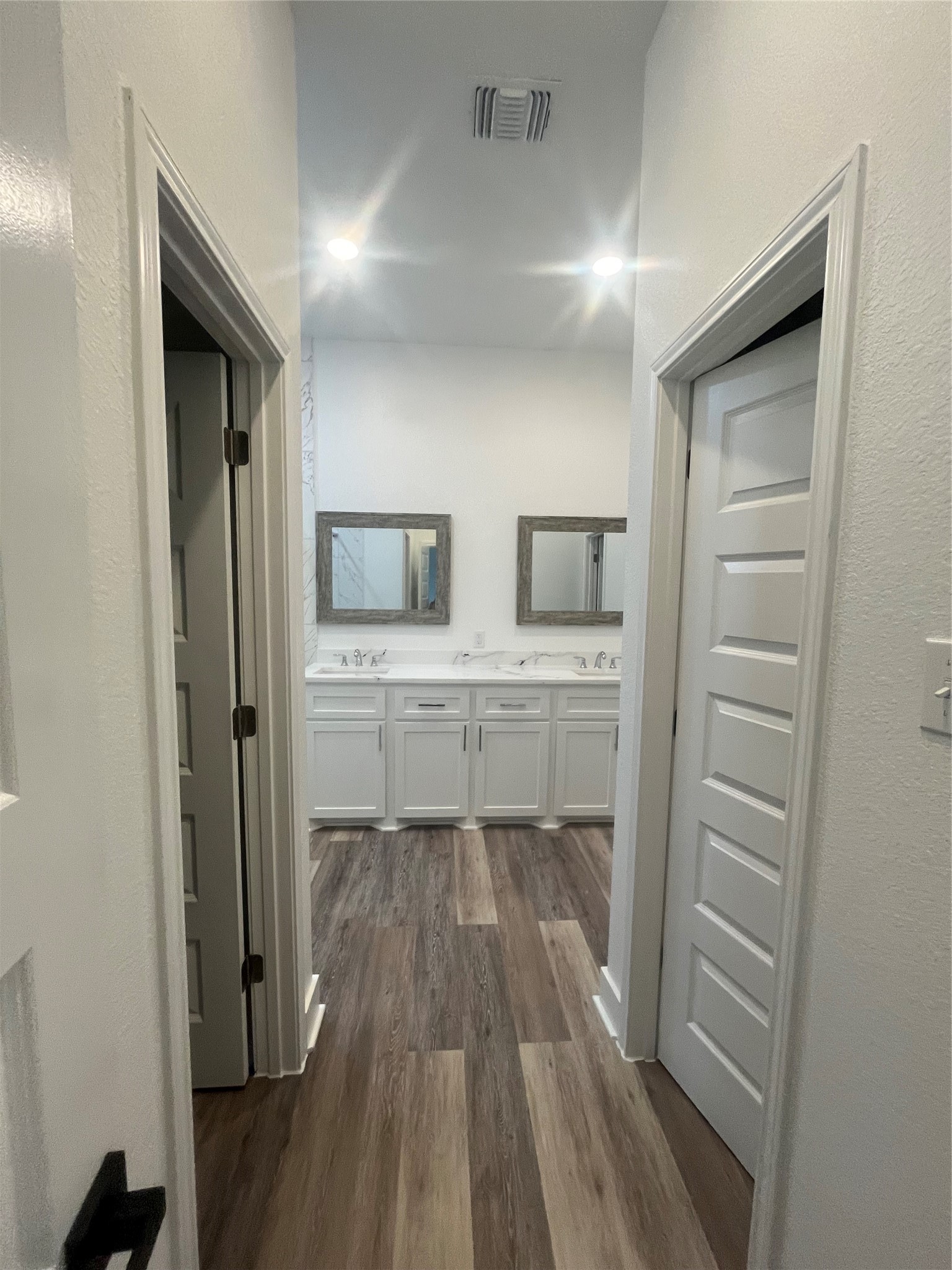 33416 FM 521 Road Angleton, TX 77515 - Photo 14 of 21 This photo showcases a modern bathroom with dual sinks, white cabinetry, and a clean, bright aesthetic. It features medium gray/ wood waterproof plank flooring and recessed lighting, creating a spacious and inviting atmosphere. Includes his and her walk-in-closets.