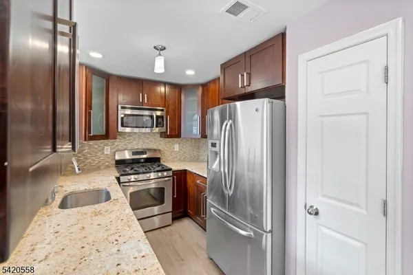 a kitchen with granite countertop stainless steel appliances a refrigerator a stove top oven and sink