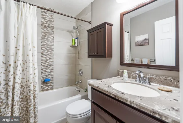 a bathroom with a granite countertop sink a toilet a mirror a bathtub and shower