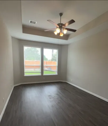 an empty room with wooden floor fan and windows