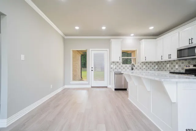 a large kitchen with kitchen island a sink dishwasher a stove a refrigerator with white cabinets and wooden floor