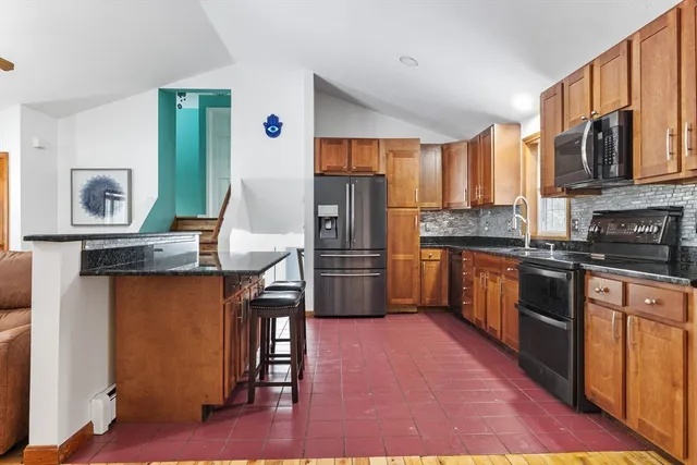 a kitchen with stainless steel appliances kitchen island granite countertop a refrigerator a stove top oven a sink dishwasher and wooden cabinets with wooden floor