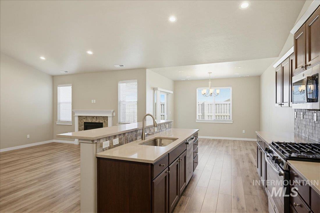 12460 West Azure Street Boise, ID 83713 - Photo 12 of 34 Open-concept kitchen featuring dark wood cabinetry, stainless steel appliances, light-toned countertops, and a tiled backsplash
