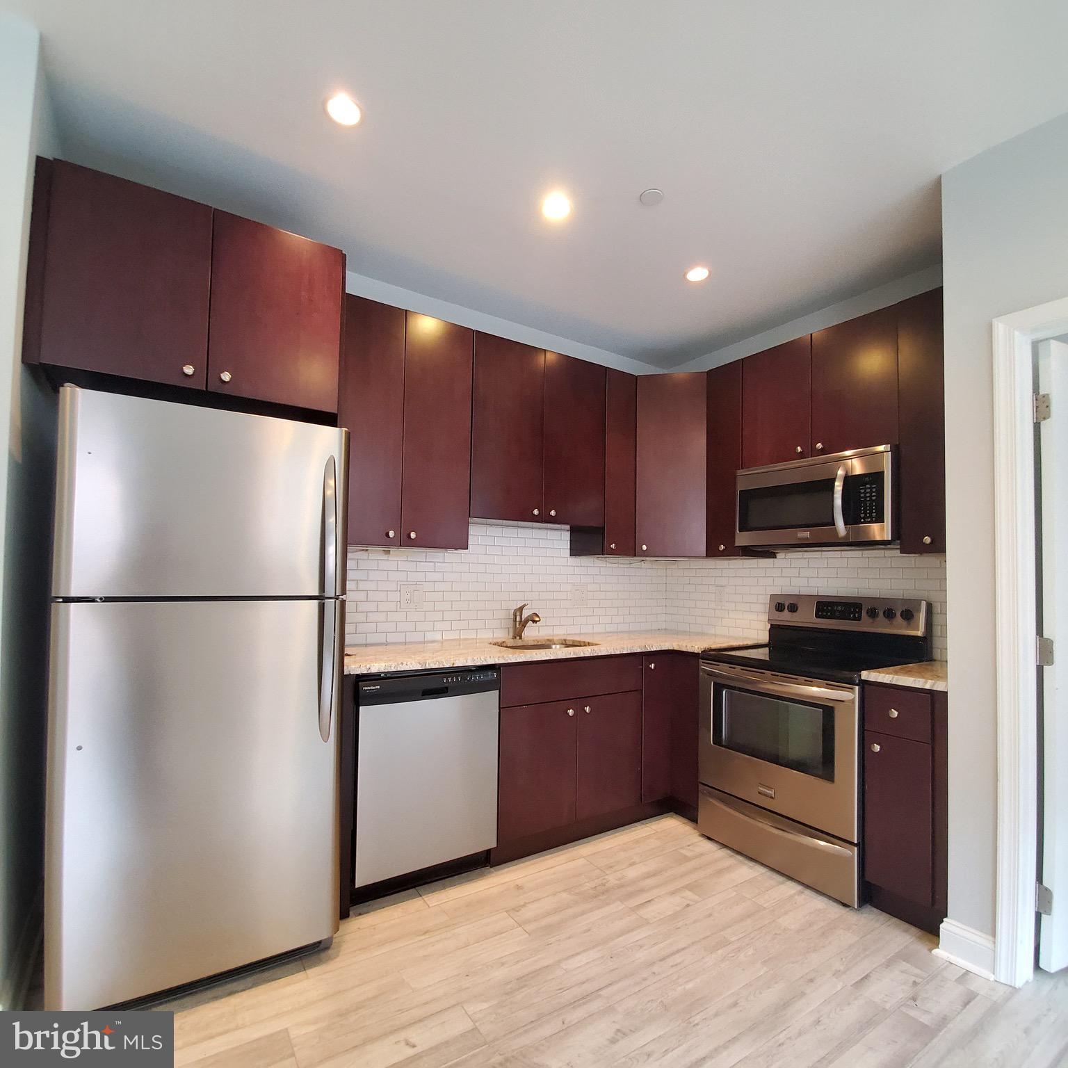 421-429 Monroe Street, Unit 102 Philadelphia, PA 19147 - Photo 3 of 10 a kitchen with stainless steel appliances granite countertop a refrigerator a sink a stove a microwave and island