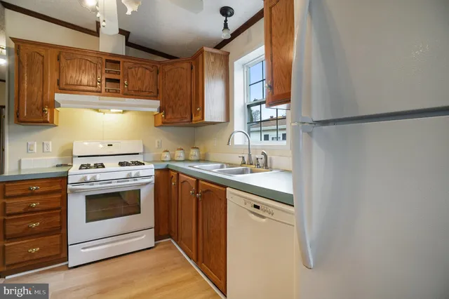 a kitchen with stainless steel appliances granite countertop a refrigerator a sink dishwasher a stove and white countertops with wooden floor