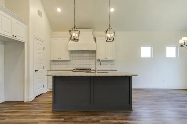 a kitchen with kitchen island granite countertop a sink cabinets and wooden floor