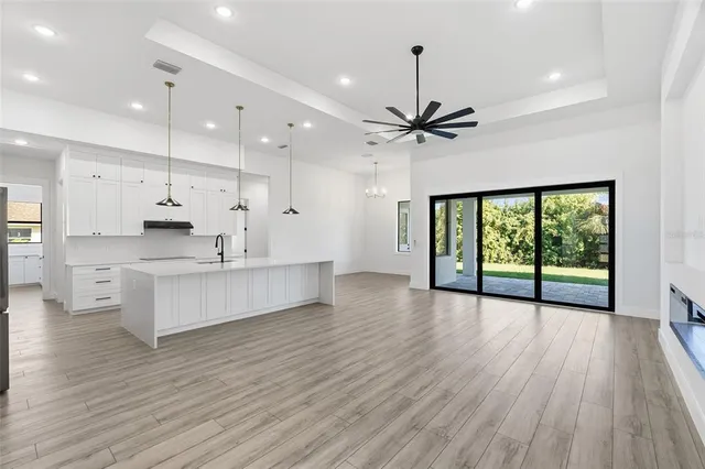 a large kitchen with stainless steel appliances granite countertop a stove a refrigerator a sink and a large window with wooden floor