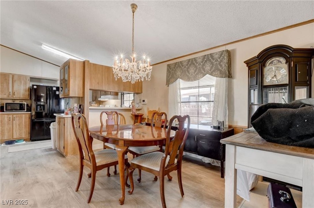 5576 Aldama Road Las Vegas, NV 89122 - Photo 11 of 23 Dining room featuring light wood finished floors, a chandelier, lofted ceiling, a textured ceiling, and ornamental molding