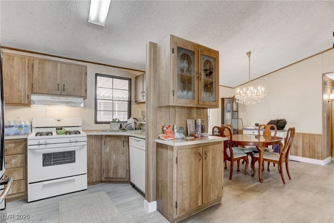 5576 Aldama Road Las Vegas, NV 89122 - Photo 13 of 23 Kitchen with white appliances, crown molding, light countertops, under cabinet range hood, and a textured ceiling