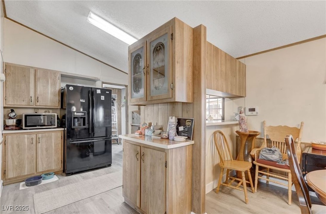 5576 Aldama Road Las Vegas, NV 89122 - Photo 14 of 23 Kitchen featuring light brown cabinetry, black fridge with ice dispenser, lofted ceiling, and a textured ceiling