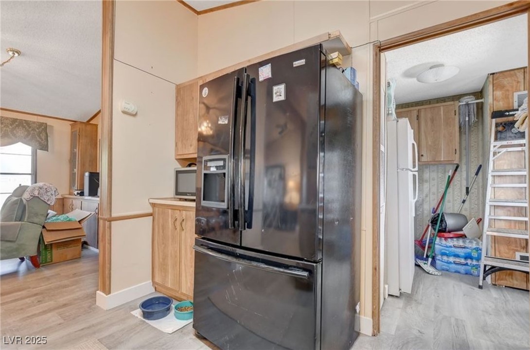5576 Aldama Road Las Vegas, NV 89122 - Photo 15 of 23 Kitchen with black refrigerator with ice dispenser, light wood-style floors, freestanding refrigerator, a textured ceiling, and ornamental molding