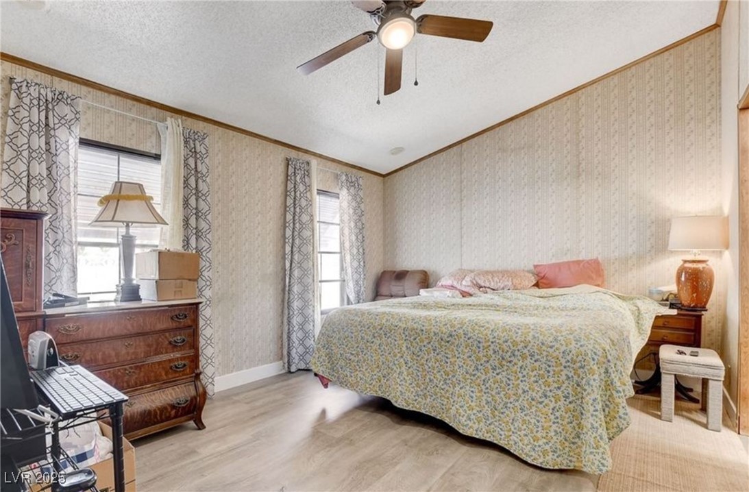 5576 Aldama Road Las Vegas, NV 89122 - Photo 16 of 23 Bedroom featuring crown molding, a textured ceiling, wallpapered walls, light wood finished floors, and a ceiling fan