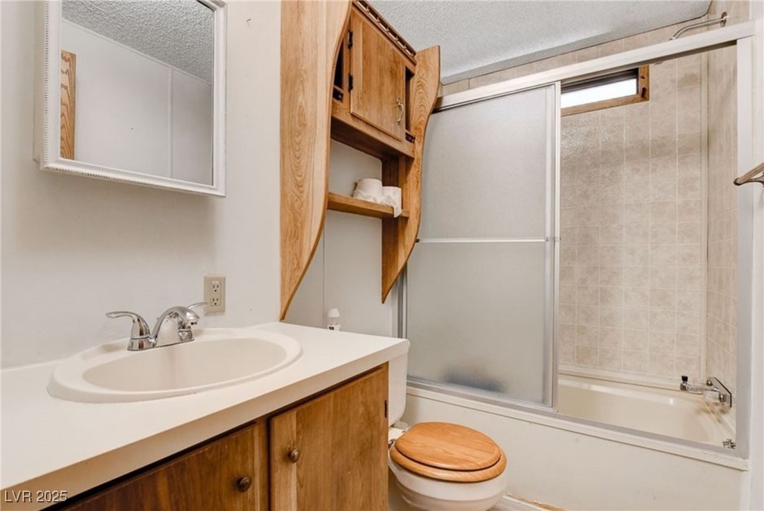 5576 Aldama Road Las Vegas, NV 89122 - Photo 19 of 23 Bathroom featuring vanity, bath / shower combo with glass door, and a textured ceiling