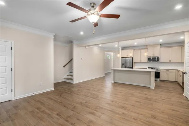 a large kitchen with stainless steel appliances kitchen island granite countertop a stove a sink a refrigerator and white cabinets with wooden floor