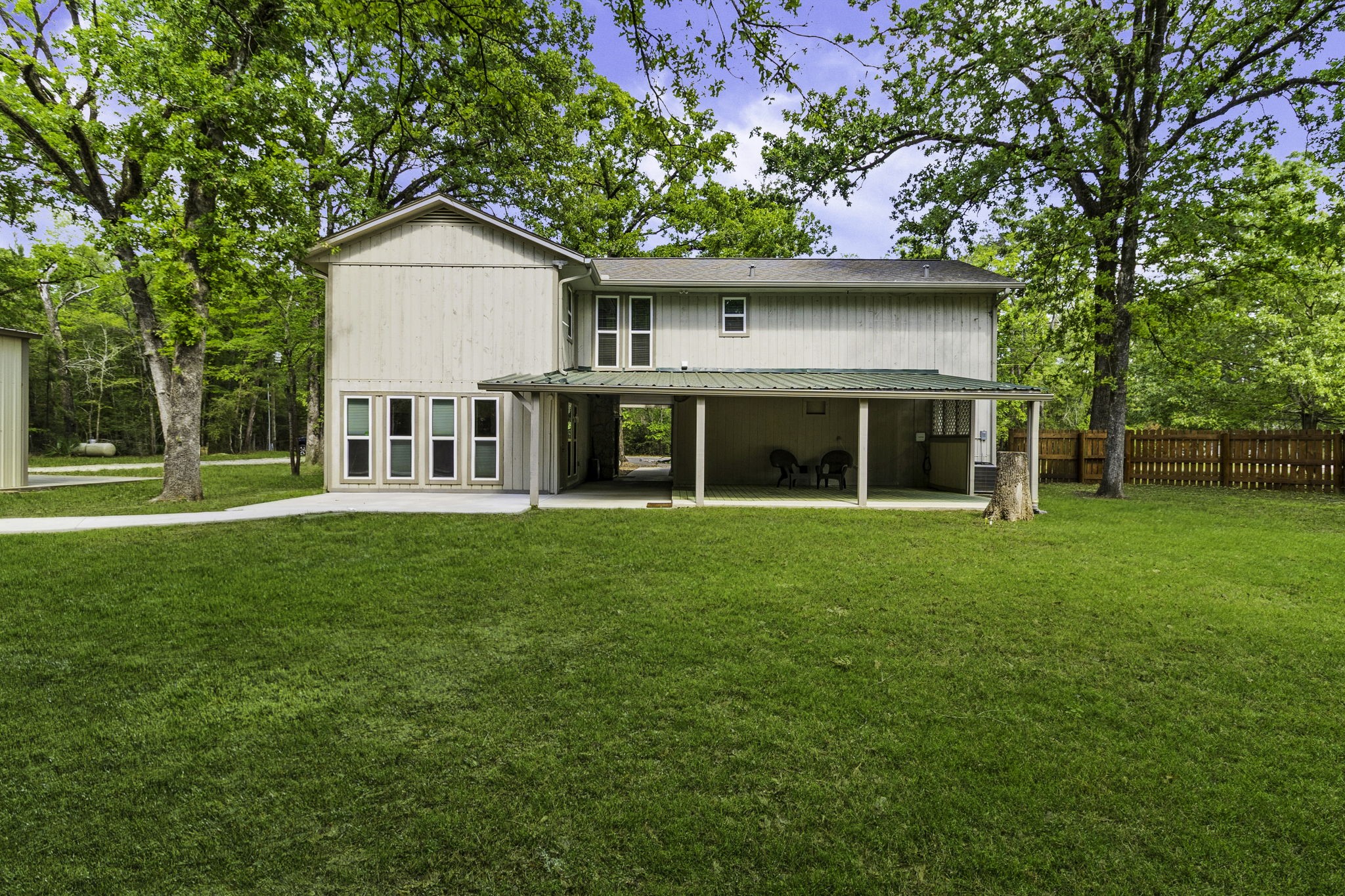 21 Red Oak Circle Point Blank, TX 77364 - Photo 24 of 32 This photo features a two-story home with a rustic exterior, nestled among mature trees. It includes a covered outdoor area and a spacious, well-maintained lawn, offering a serene and private setting.