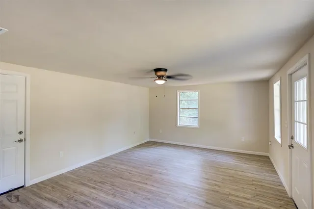 an empty room with wooden floor chandelier fan and windows