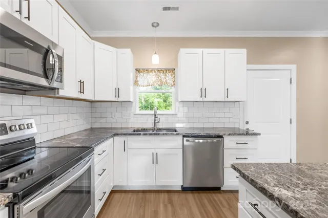 a kitchen with stainless steel appliances granite countertop a kitchen island a stove a sink and white cabinets
