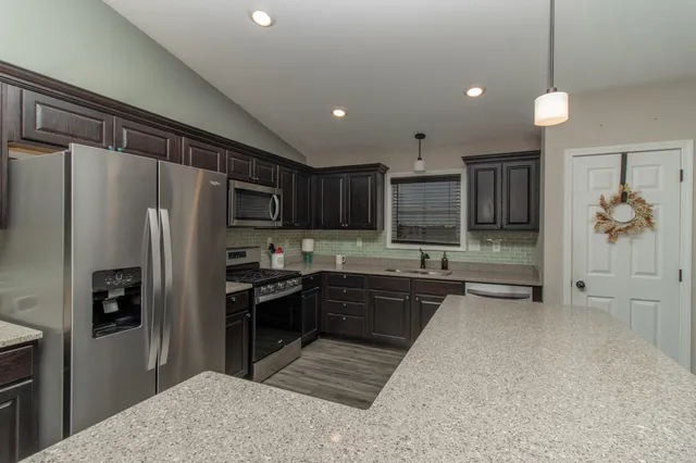 a kitchen with stainless steel appliances granite countertop a refrigerator a sink dishwasher a stove and white cabinets with wooden floor