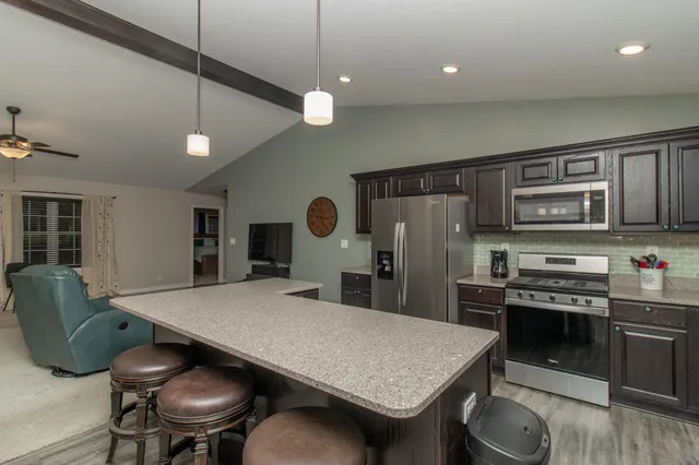 a kitchen with stainless steel appliances granite countertop a stove a refrigerator a sink a dining table and chairs with wooden floor