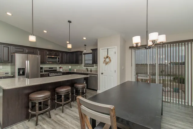 a kitchen with stainless steel appliances granite countertop a refrigerator a sink dishwasher a dining table and chairs with wooden floor