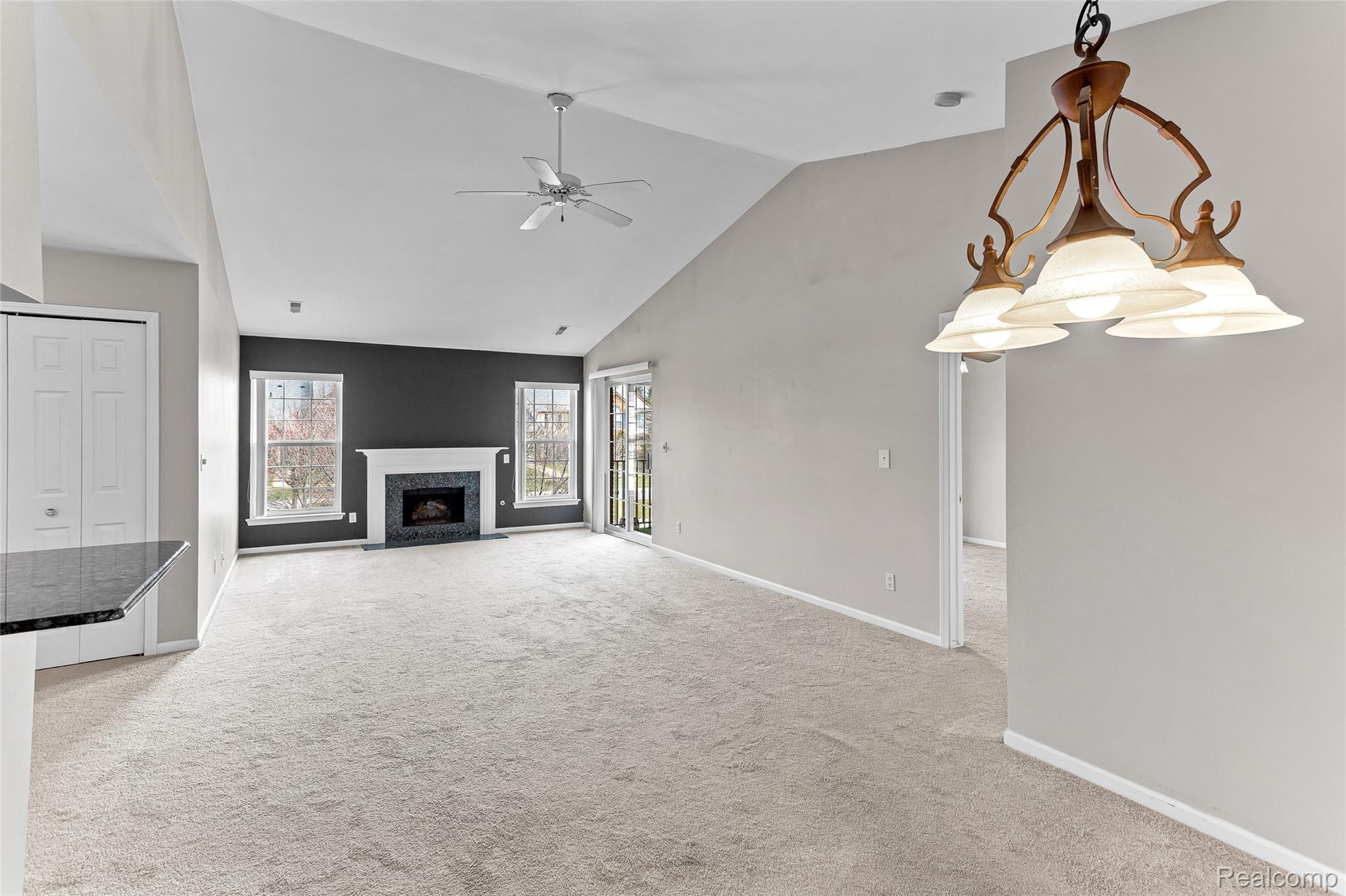3553 Oakmonte Boulevard Rochester, MI 48306 - Photo 8 of 42 Spacious living area featuring a vaulted ceiling with a ceiling fan, a fireplace with a black surround, and light carpeting throughout