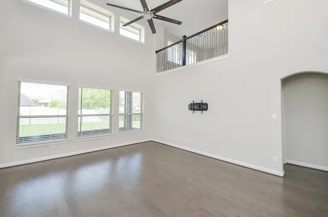 an empty room with wooden floor fan and windows