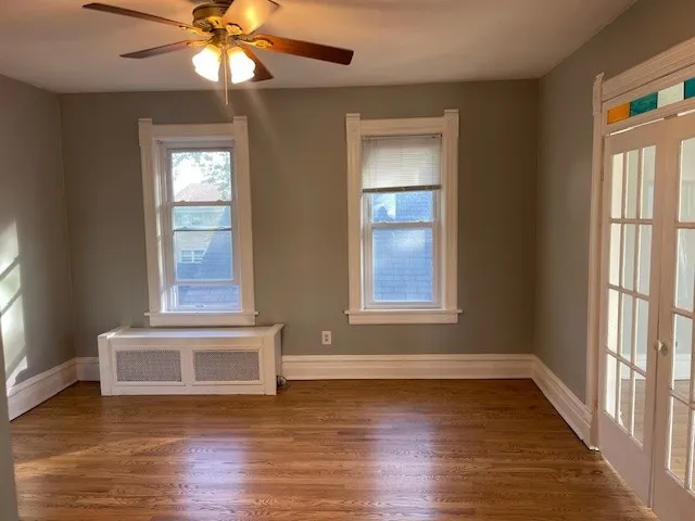 an empty room with wooden floor fan and windows