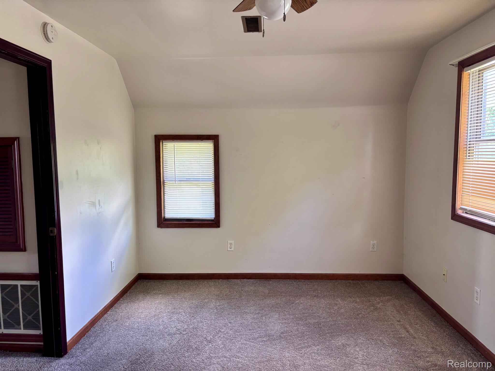 Carpeted flooring, vaulted ceiling, and two windows with blinds