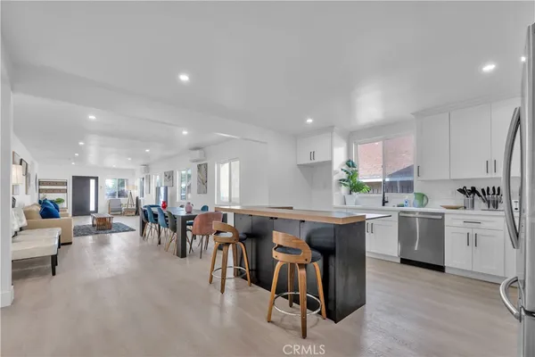 a large dining hall with stainless steel appliances lots of white furniture a window and kitchen view